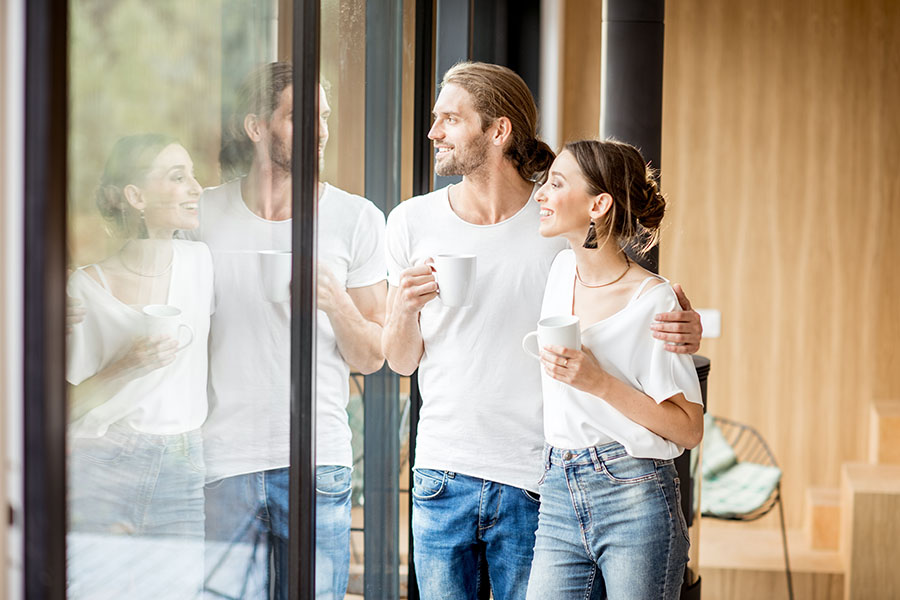 Insurance Quote - Young Couple Drinking Coffee and Looking Outside from the Glass Doors Inside Their Modern Home