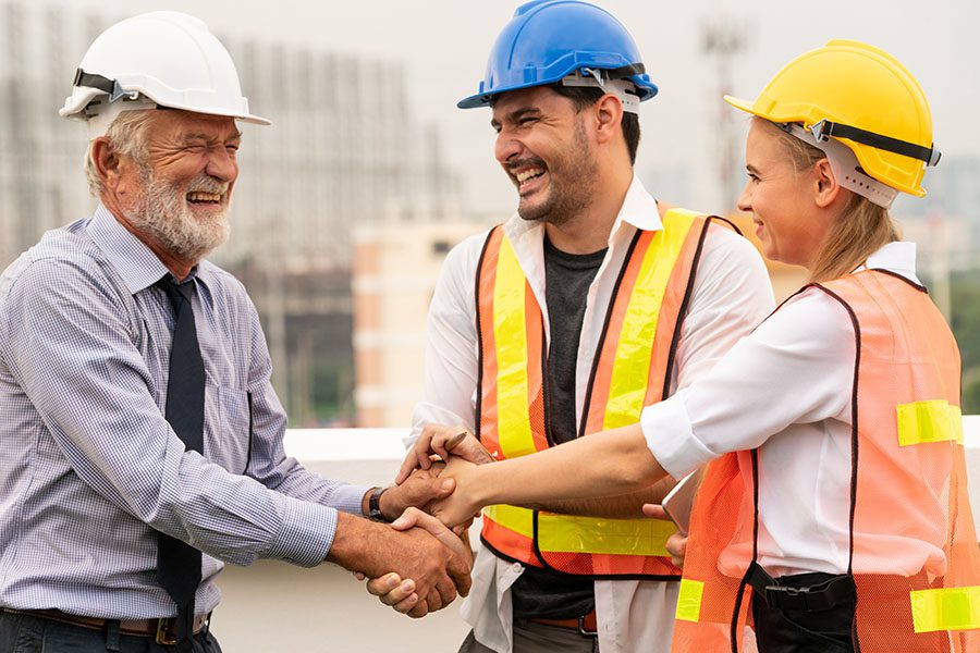 Specialized Business Insurance - Engineer and Two Smiling Contractors Standing on a Construction Jobsite Shaking Hands to Celebrate Success