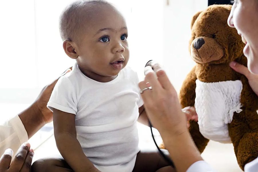 Individual Health Insurance - Baby during a Doctor Visit for a Wellness Checkup with the Doctor Holding a Childs Teddy Bear to Try and Keep Childs Attention and to Stay Positive