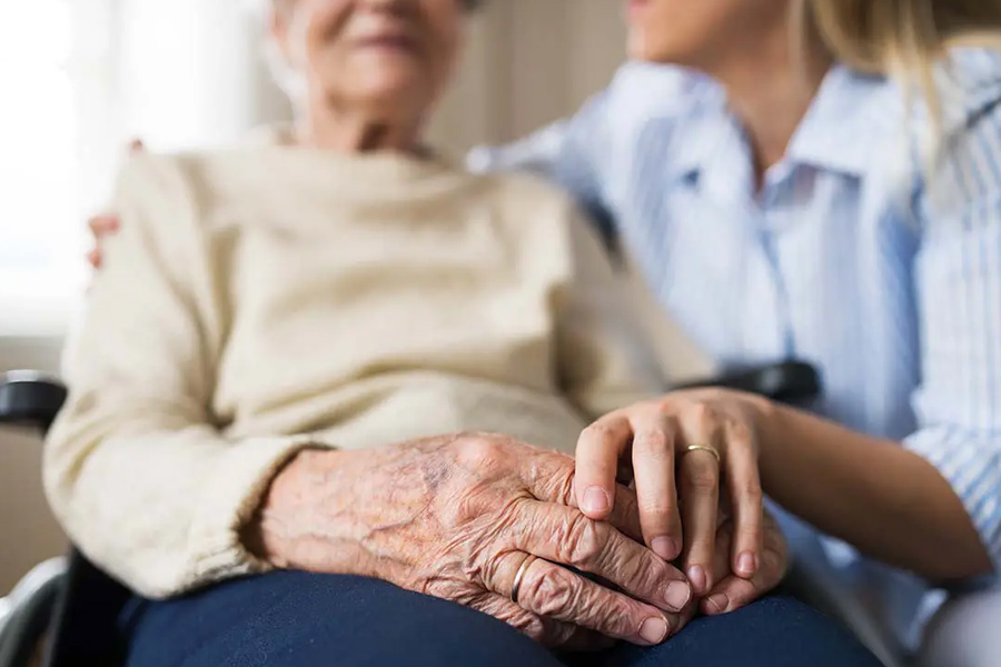 Long-Term-Care-Insurance-Close-up-of-a-Senior-Woman-in-a-Wheelchair-with-a-Focus-on-Her-Hands-Sitting-with-a-Health-Care-Worker-at-a-Senior-Care-Facility